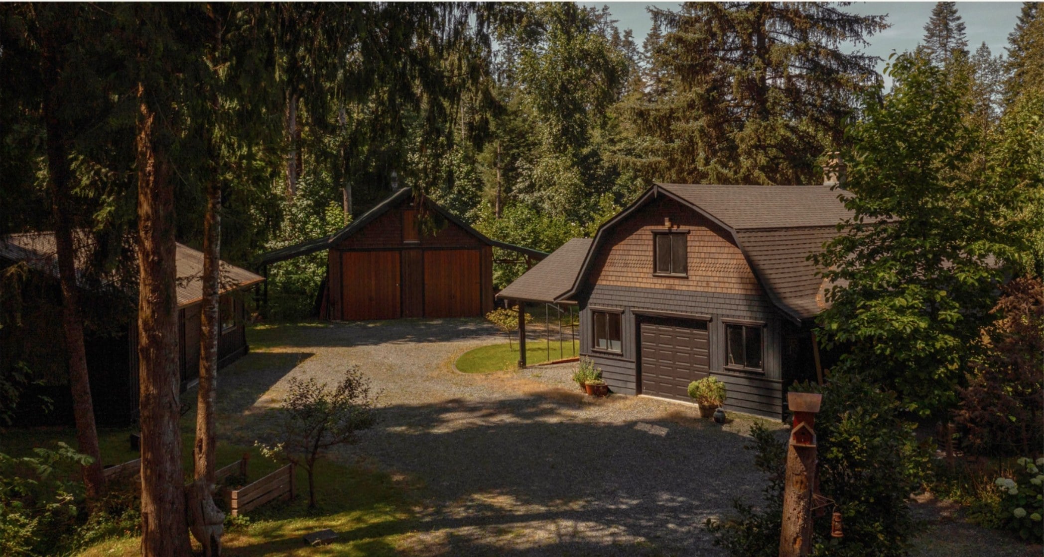 The barn and house among tall firs, seen from above the gravel drive
