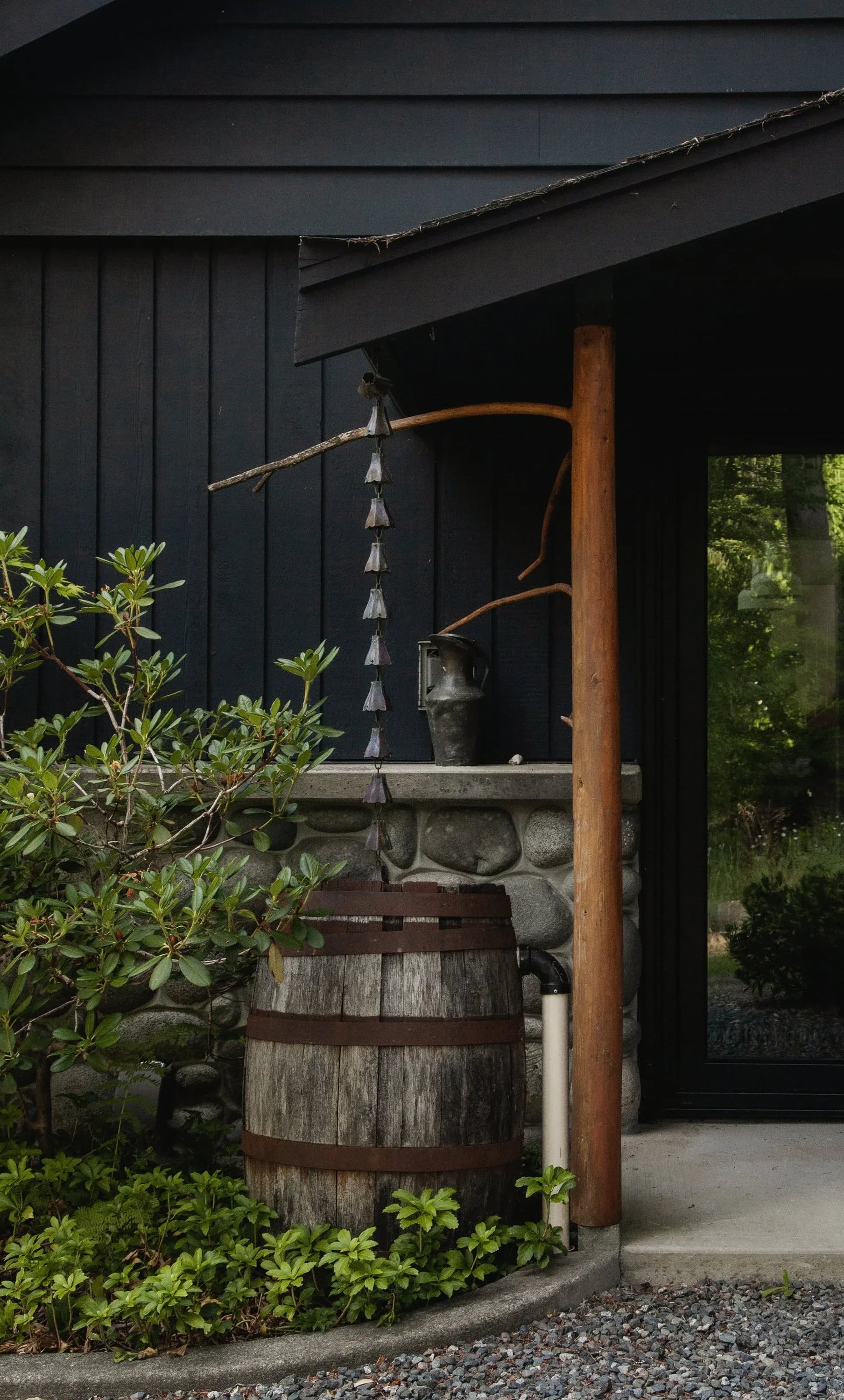 A dark timber entrance with a rain chain and a wooden barrel