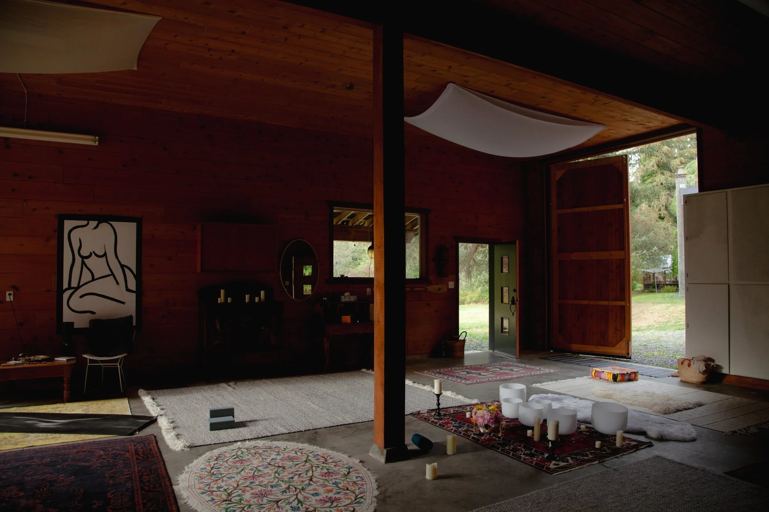 The barn floor laid with rugs and singing bowls, its doors open to the garden