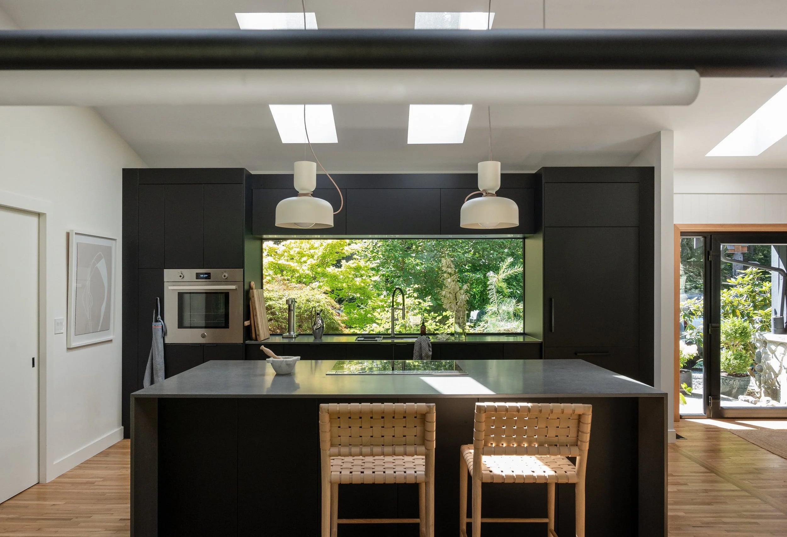 A black kitchen island with stools, the garden through the window behind