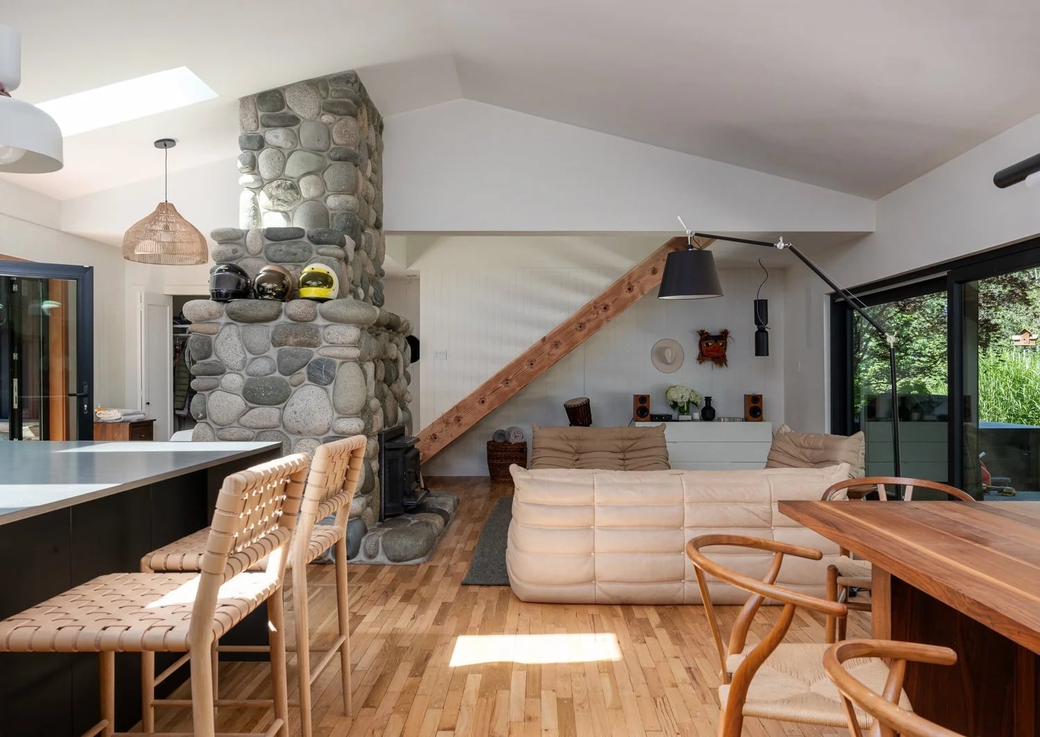 An open living room with a stone fireplace and wooden stairs