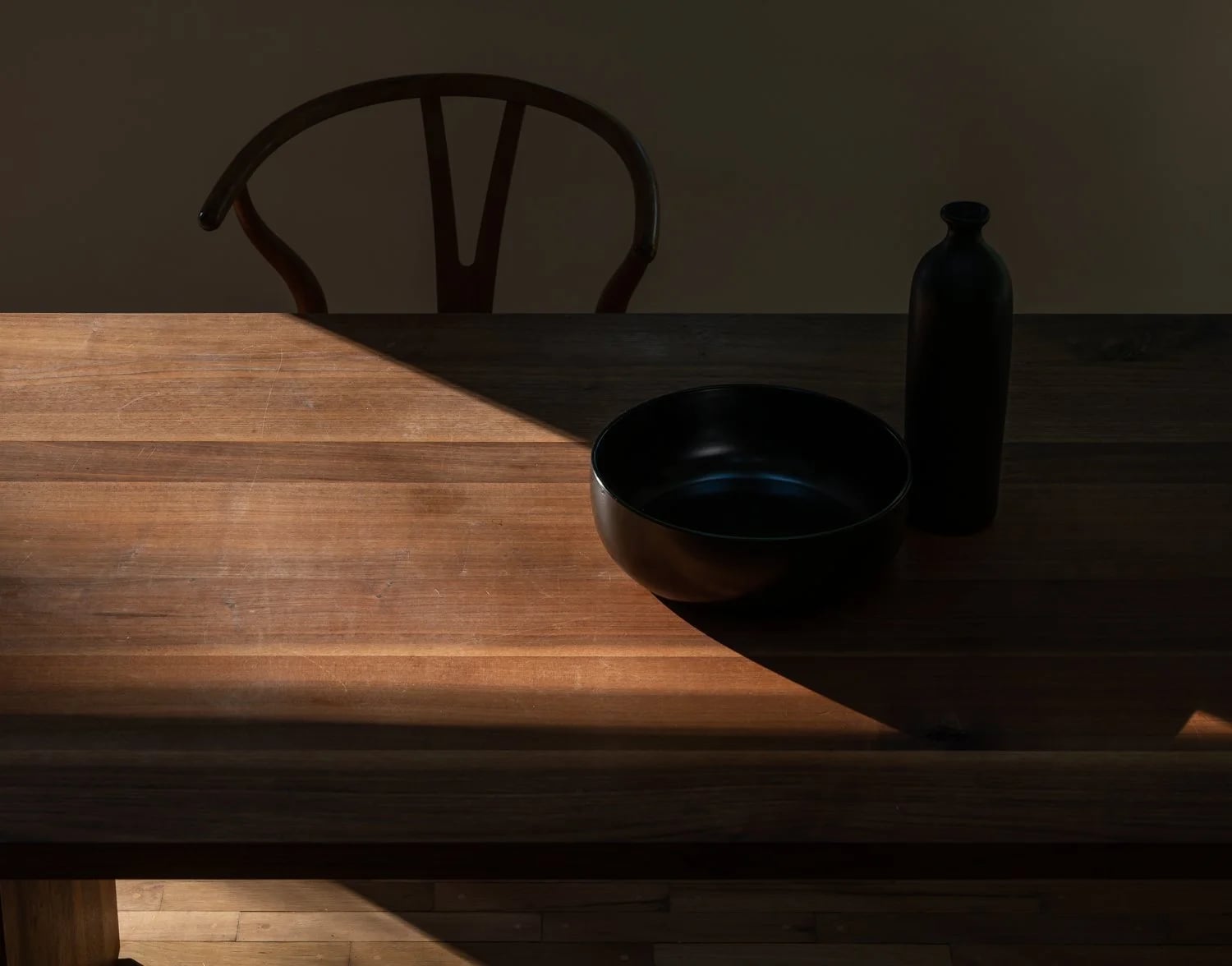 Sunlight across a wooden table and a black bowl