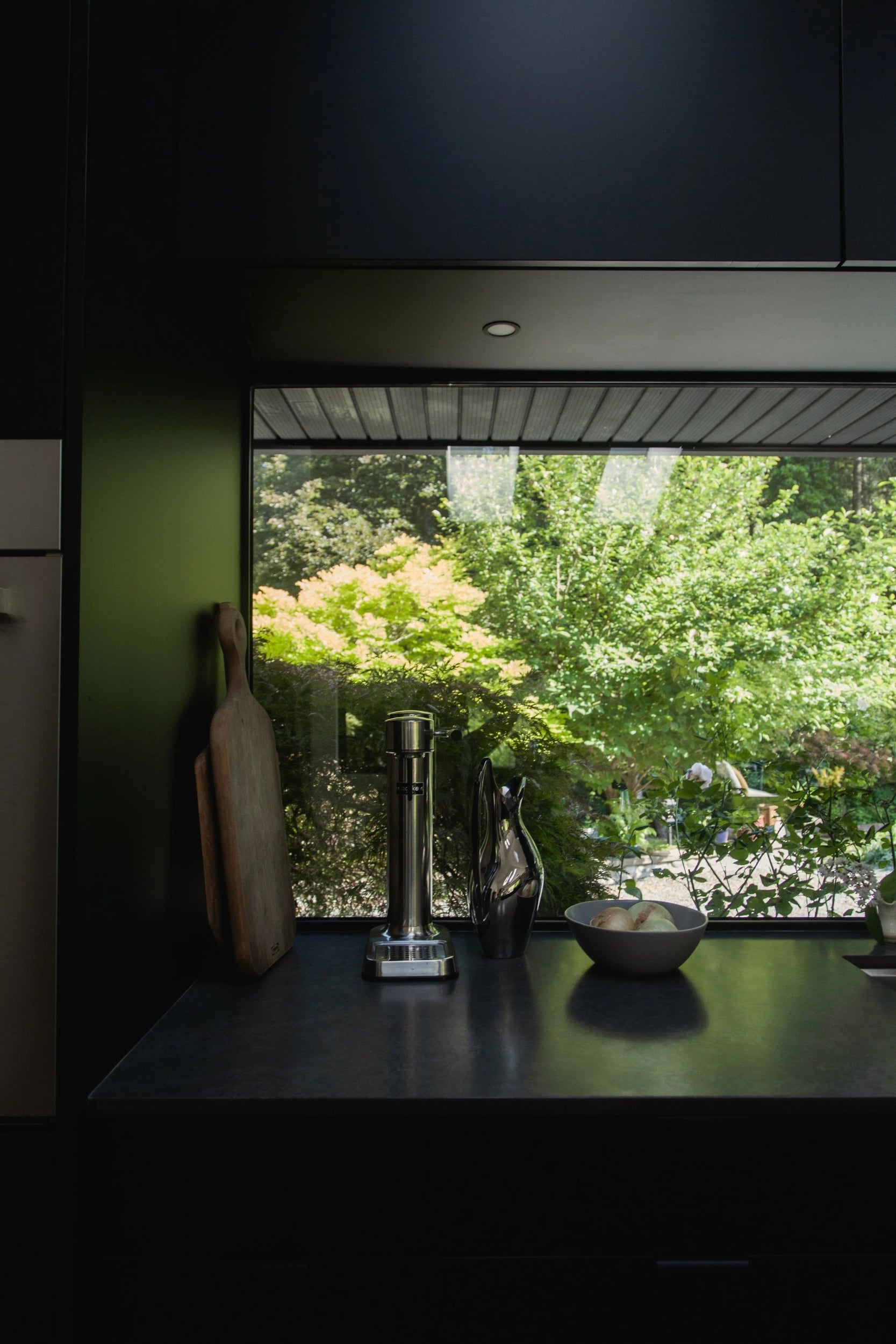 A dark room opening onto bright green maples through a wide window