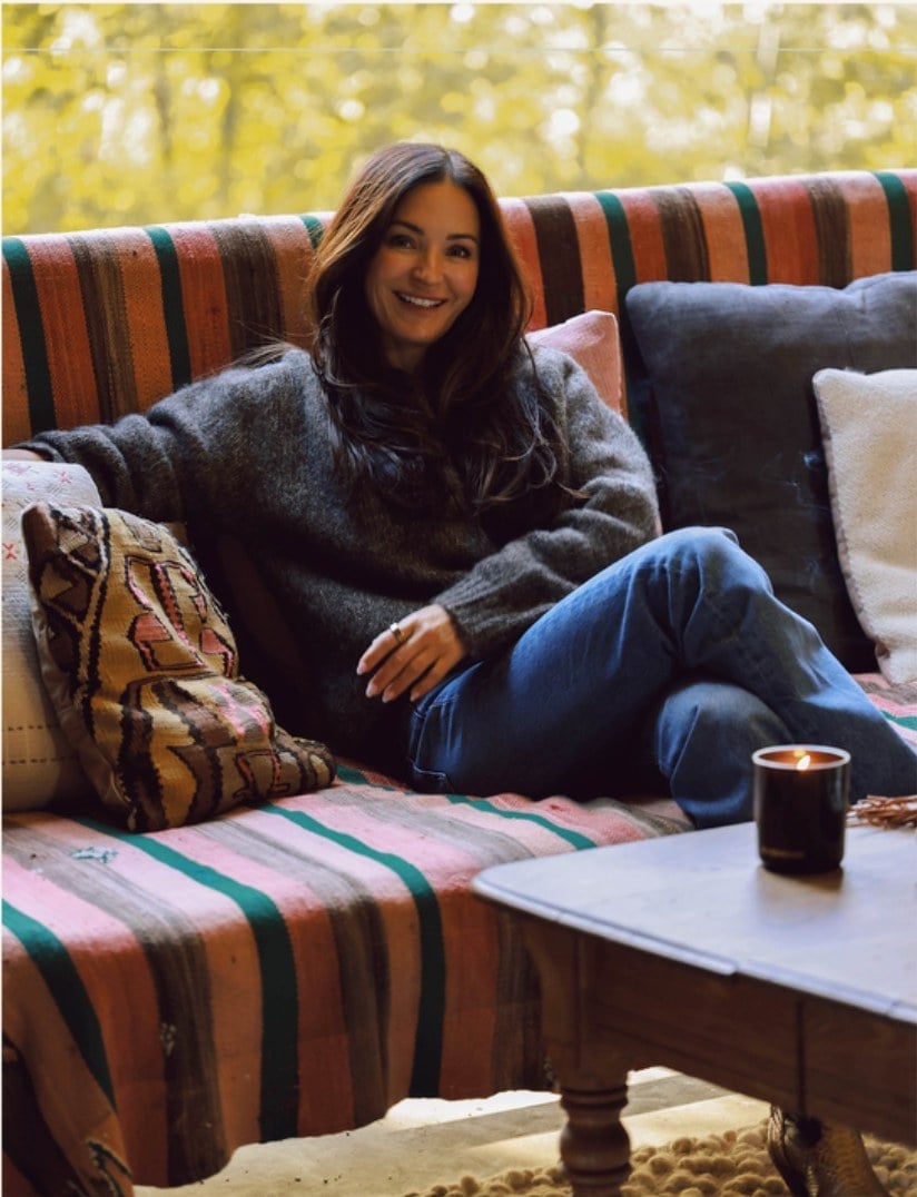 Katie Burkard on a striped sofa, a candle on the table beside her