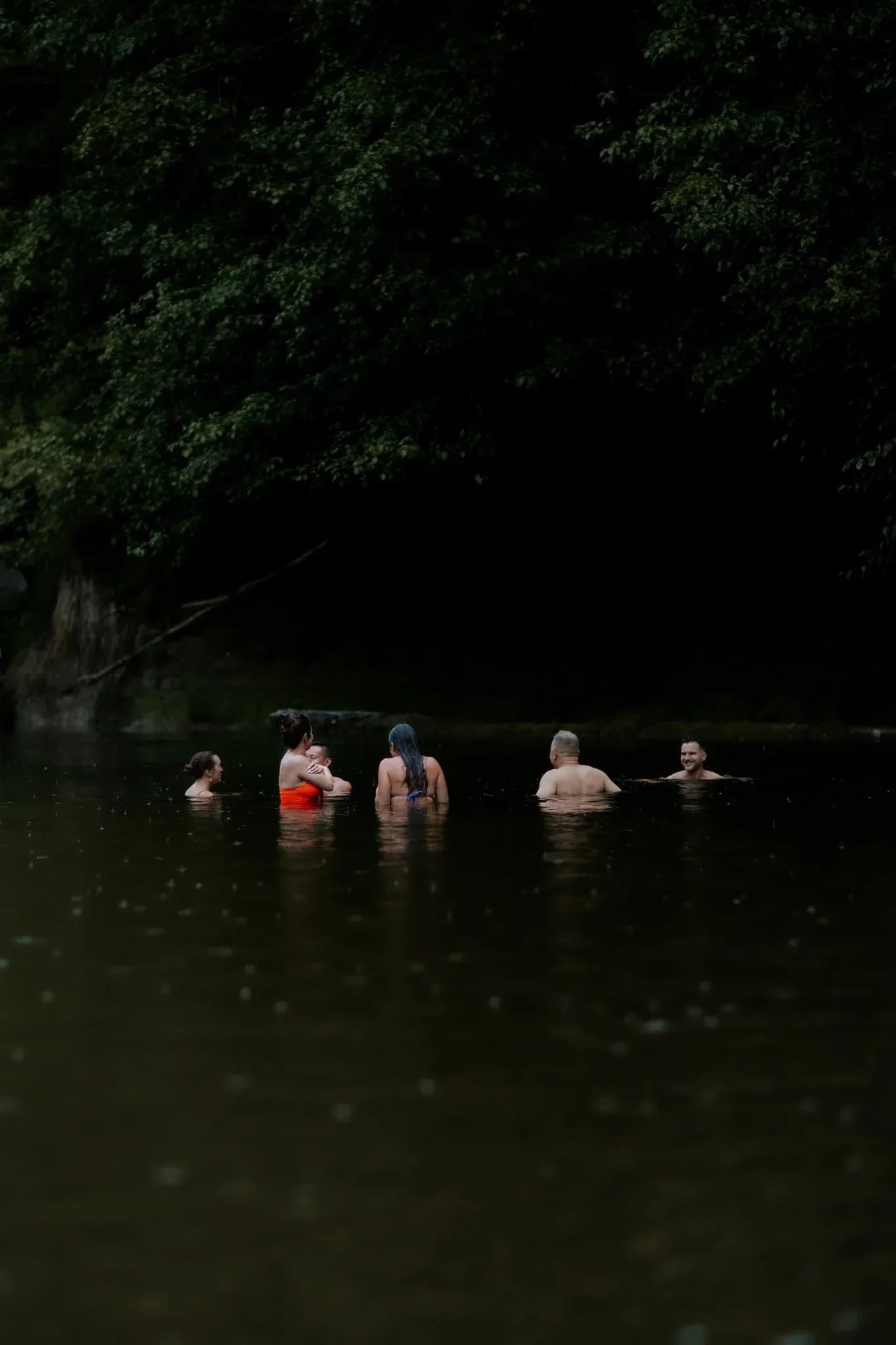 A group swimming in the river under dark trees