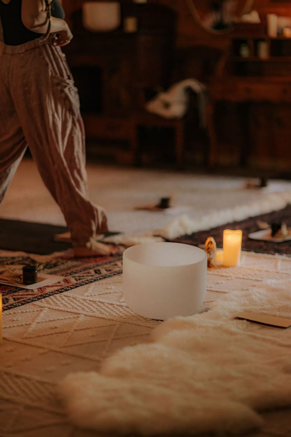 A crystal singing bowl on a rug beside a candle